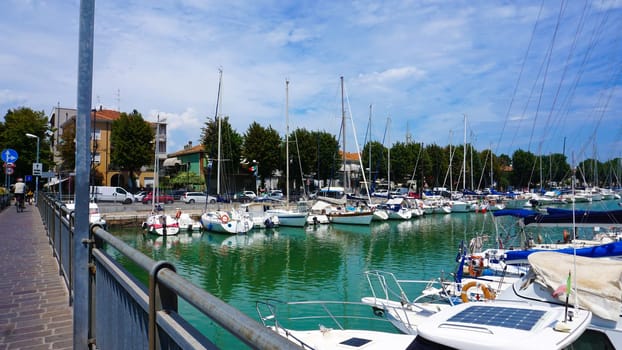 Summer view of pier with ships, yachts and other boats with ferris wheel in Rimini, Italy.
