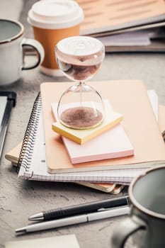 Crop of hourglass on home office table count measure time.  Workplace of busy employee, time management and burnout concept