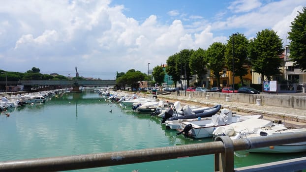 Rimini, Italy - June 25, 2024: Summer view of pier with ships, yachts and other boats with ferris wheel in Rimini, Italy.
