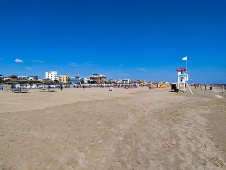 Rimini, Italy - June 25, 2024: People going along Rimini beach. The sunbeds and parasols on the beach