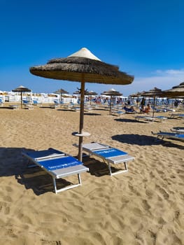 Rimini, Italy - June 25, 2024: People going along Rimini beach. The sunbeds and parasols on the beach