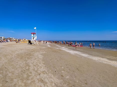 Rimini, Italy - June 25, 2024: People going along Rimini beach. The sunbeds and parasols on the beach