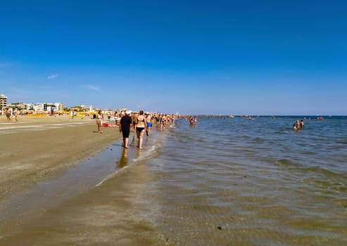 Rimini, Italy - June 25, 2024: People going along Rimini beach. The sunbeds and parasols on the beach