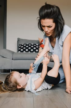Mother dressing her playful daughter in their cozy living room, bonding over parenthood and creating childhood memories filled with laughter and togetherness