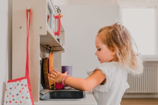 Young girl happily plays in a cozy playroom with her colorful toy kitchen. Using her imagination to cook and wash dishes. Fully immersed in her pretend world