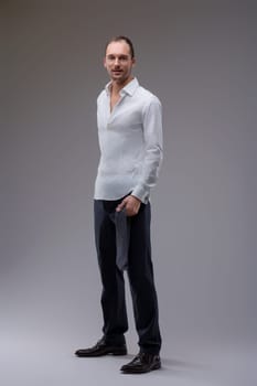 Young businessman is holding his tie in his hand after a long day of work, he is wearing a white shirt and blue pants