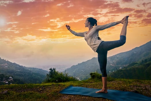 Woman doing yoga asana Natarajasana Lord of the dance pose outdoors at in Himalayas