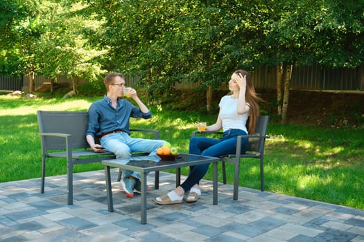 Father and daughter are sitting at a patio table with refreshing drinks on a sunny day in the backyard