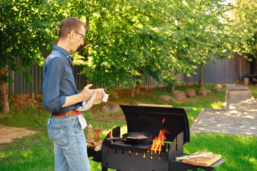 Middle-aged man man wiping his hands with a towel while standing at the grill in the backyard