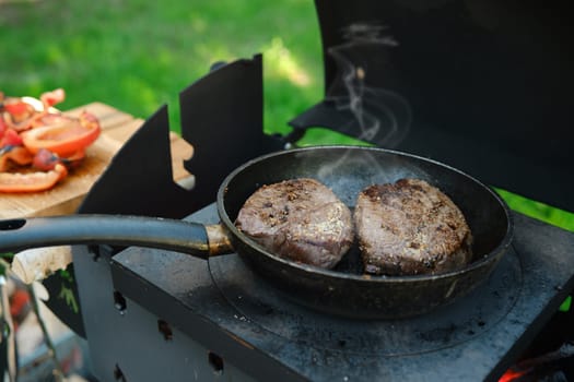 Two pieces of beef steak in a frying pan on outdoor grill