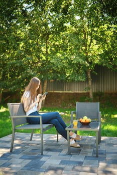 A young woman enjoys the fresh air while sitting on a bench in the backyard of her summer house