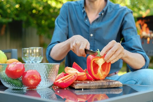 Unrecognizable man slicing red bell pepper at a barbecue picnic
