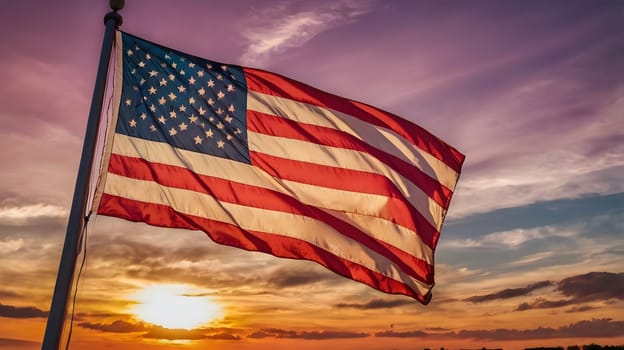The American flag is waving proudly in the wind as the sun sets behind it, casting a warm glow on the sky. The flag is seen in full, with its red, white, and blue stripes and stars, billowing in the breeze. The sky behind it is a blend of orange, purple, and blue, creating a striking contrast with the flag.