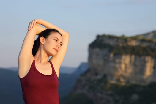 Serious asian woman stretching arms in nature at sunset