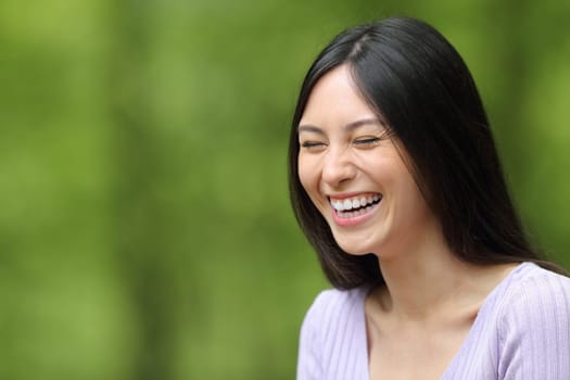 Happy asian woman laughing in a park on green background