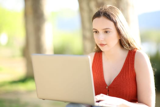 Serious woman in red using laptop sitting in a park