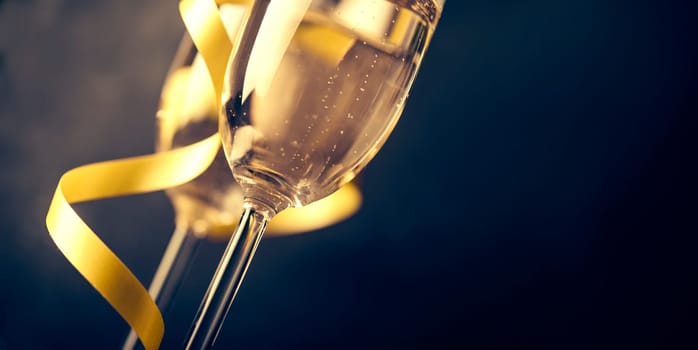 Two champagne glasses with golden ribbon on dark background with copyspace. Luxury restaurant dinner celebration. Classy christmas and new year holiday panoramic design banner.