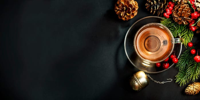 Christmas tea and christmas decoration on black background from above. Cozy winter hot beverage and december pine cones decor on dark table. Top view.