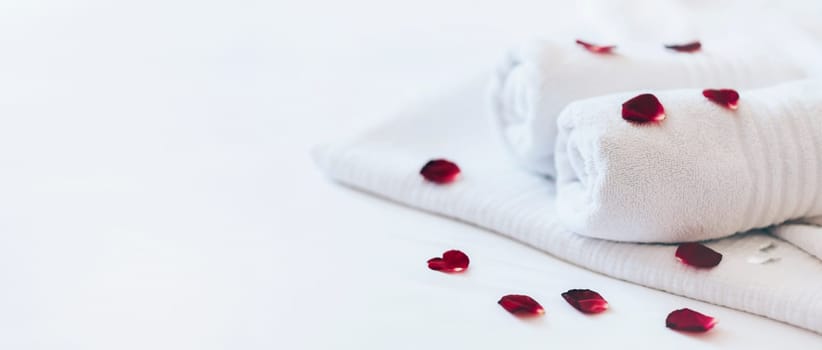 Luxury hotel room with white spa towels on bed sheet with rose petals. Romantic holiday weekend with wellness body treatment  and relax couple massage in honeymoon suite. Closeup.