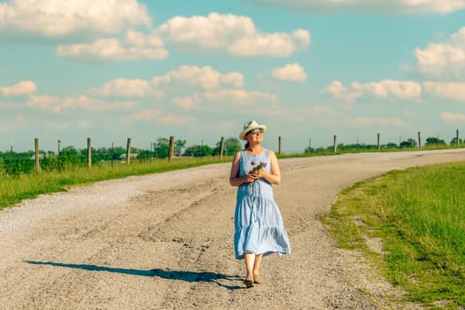 Happy mature woman is walking along a rural road on a bright summer day.
