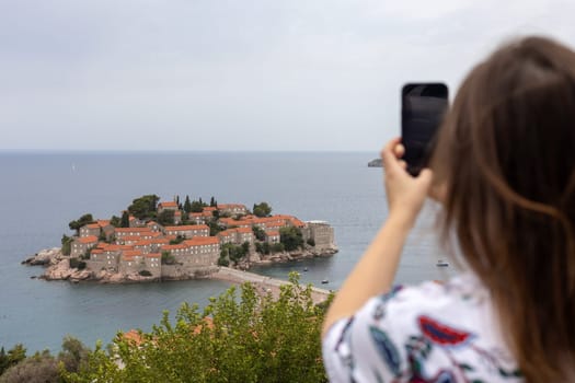 Montenegro, Budva June 26, 2024 , a tourist takes pictures on her phone of the island of Sveti Stefan, located on the Adriatic coast of Montenegro