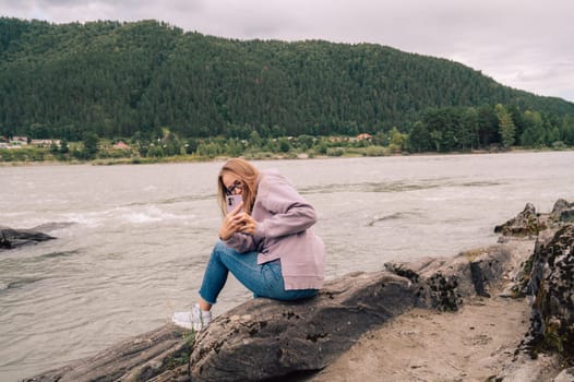 Woman at the river Katun at summer day. Taking photo on her smartphone