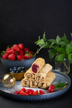 Crepes stacked in a pile, one of which is cut and filled with berry filling. The plate is also decorated with blueberries, strawberries, and cherries