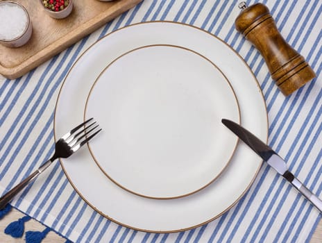 Round empty white ceramic plate, knife and fork on the table, top view