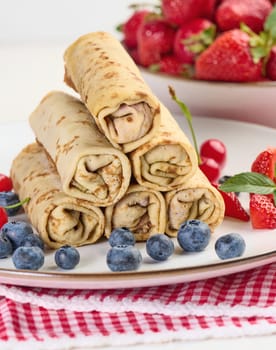 Stack of fried crepes with filling on a round plate, white table
