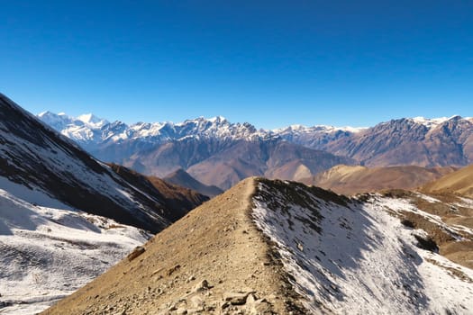 On the way from the Thorong La, Thorung La, Thorang La pass to Muktinath, the trail is running over a small ridge in front of a mountain range, Annapurna Circuit Trek, Nepal 2022
