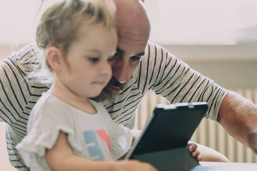 Father and daughter bonding over a digital tablet at home, smiling, laughing, and sharing happy moments in cozy living room