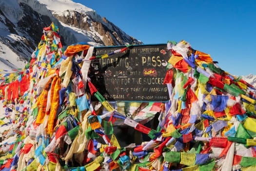 The sign marking the highest point of the Thorong, Thorung, Thorang La pass, covered by hundreds of colorful prayer flags, Annapurna Circuit Trek, Nepal 2022