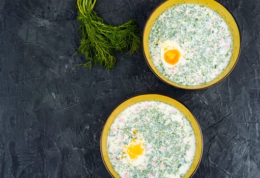 Delicious cold summer soup okroshka with boiled sausage in bowl. Top view