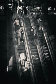 Antwerp, Belgium, July 20th 2024: Black and white verticals shot of commuters on the escalators descending towards the underground