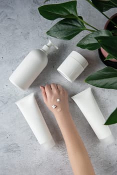 Young woman applying hand many creams at gray background