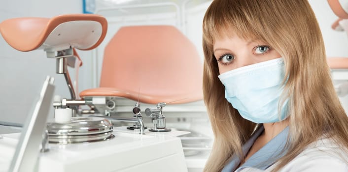 Female gynecologist in protective mask and whitecoat with gynecological vaginal retractor in hand