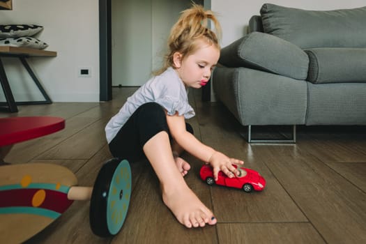 Little girl happily playing with a red toy car in her cozy living room, lost in a world of fun and imagination