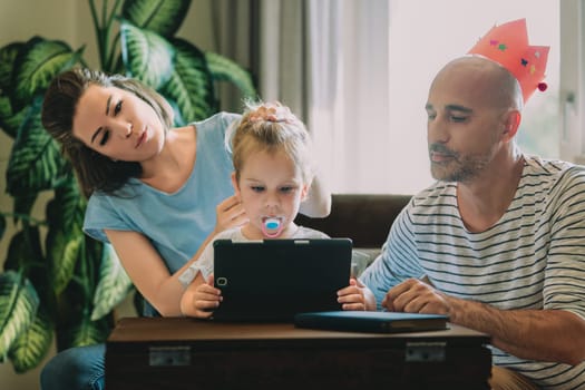 Young family is gathered around a digital tablet, enjoying quality time together while learning and playing. The parents are engaged in helping their daughter navigate the digital world