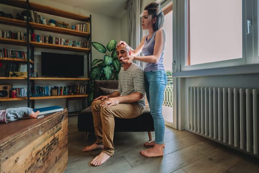 Woman applies a beauty treatment to her husband's face at home, showing love and care in their cozy living room
