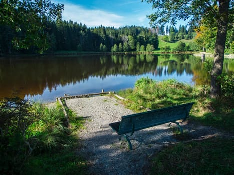 Idyllic landscape view at a small pond with a bench in summer in the Bavarian Allgäu.
