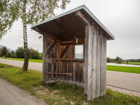Landscape view with wooden bus shelter with adjacent birch tree under overcast sky in Bavaria.