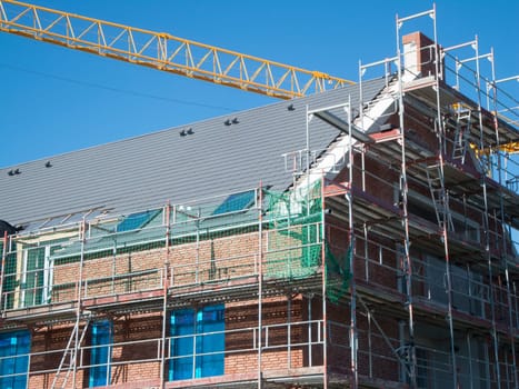 Partial view of scaffolding on a newly constructed multi-story building with brick cladding and yellow crane boom against a blue sky.
