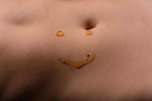 Beautiful seductive young female makes honey on a black background. Drops of honey on her belly.
