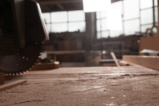 Sawdust covering a workbench with a circular saw in the foreground and a carpenter workshop out of focus in the background