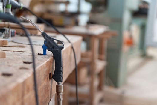 Air duster is lying on a workbench in a carpenter's workshop, with other tools and machinery in the background out of focus. The image conveys a sense of craftmanship and tradition
