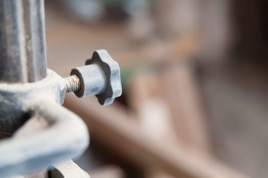 Wing nut covered in sawdust securing a piece of equipment in a workshop, with a shallow depth of field emphasizing the texture of the machinery and wood in the background