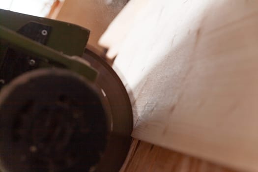 Carpenter using an electric sander on a wood plank in a workshop, creating sawdust and achieving a smooth finish. The image focuses on the tools and machinery in shallow depth of field