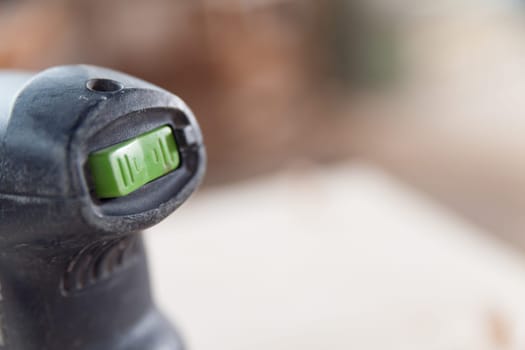 Close up view of the onoff switch and speed control of a power tool lying idle on a workbench in a workshop, with a shallow depth of field