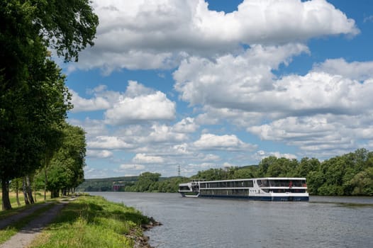 A pleasure boat sails along a river, with green nature, blue sky and white clouds