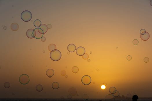 Many colorful soap bubbles float in the orange sky at sunset